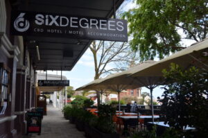 Six Degrees Albany hotel entrance sign on Stirling Terrace with outdoor seating and umbrellas in Albany, WA.
